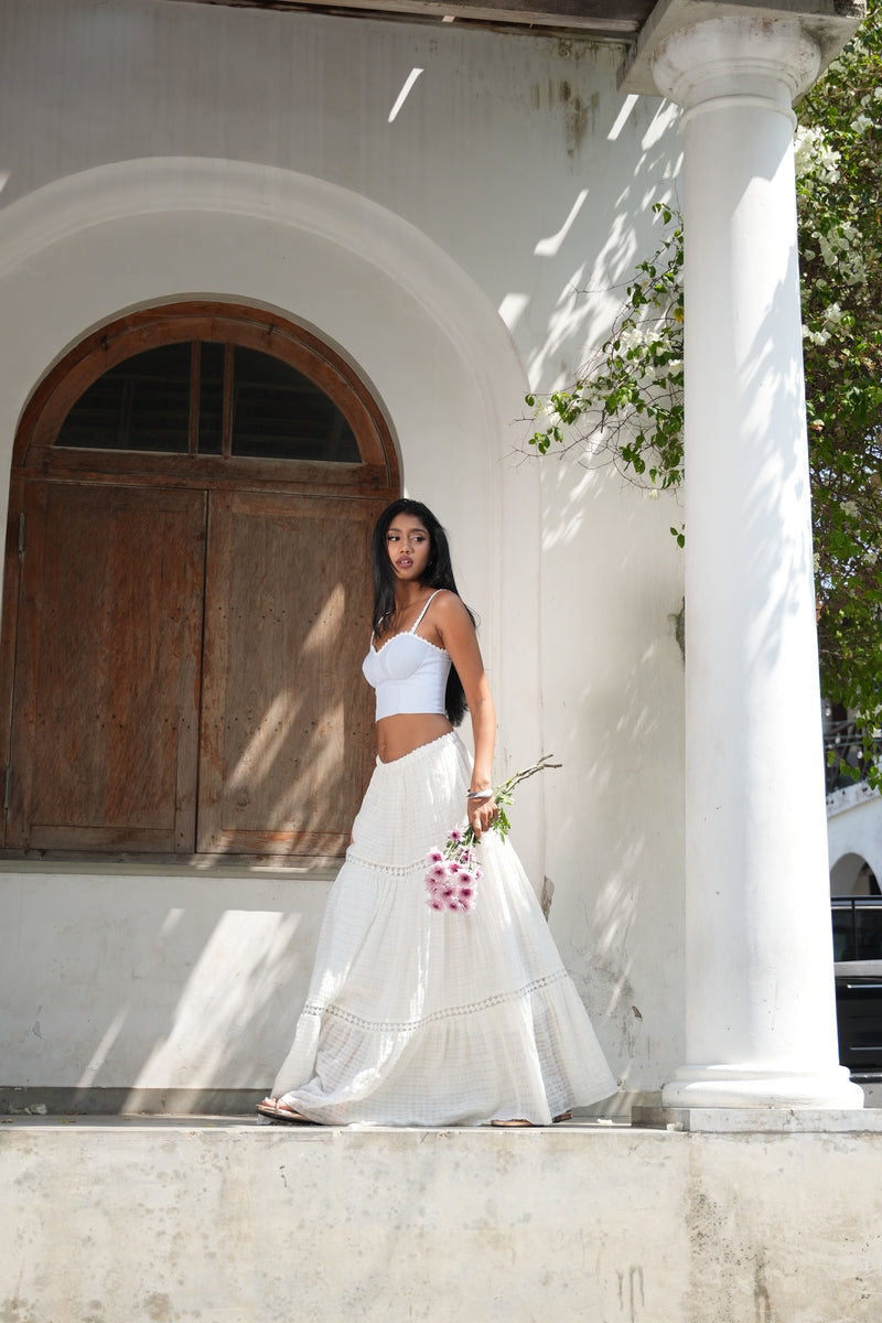 Woman in a white dress holding flowers standing in front of a wooden door.