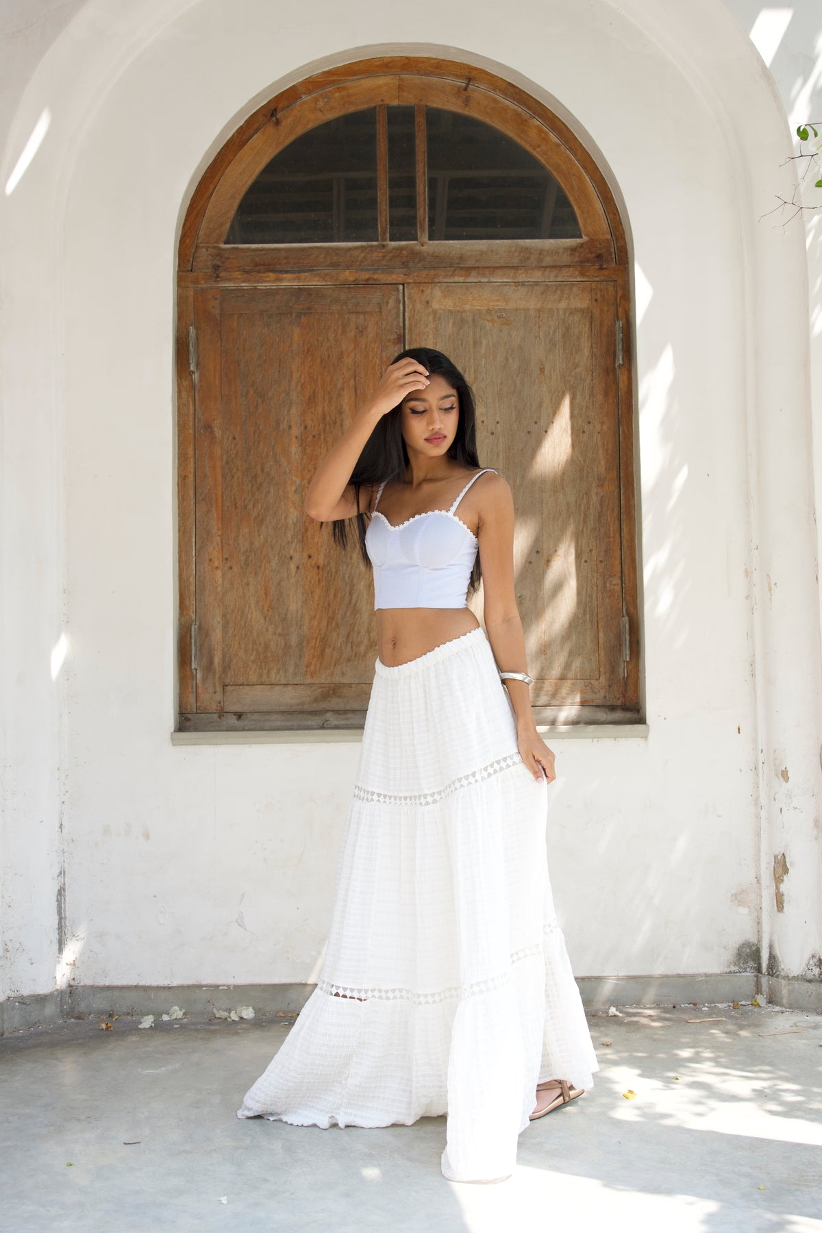 Woman in a white outfit standing in front of a wooden door.